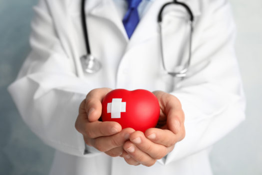 Doctor holding red heart with adhesive plasters, closeup view.