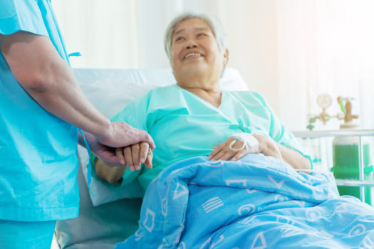 Patient in bed in medical facility holding hand of medical professional.
