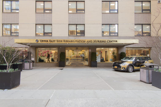 Outdoor entrance way to Upper East Side Rehabilitation and Nursing Center with smart car in view.