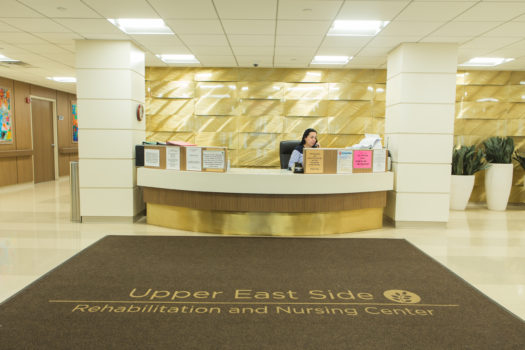 A receptionist is sitting behind the service desk in lobby at Upper East Side Rehab & Nursing Center.